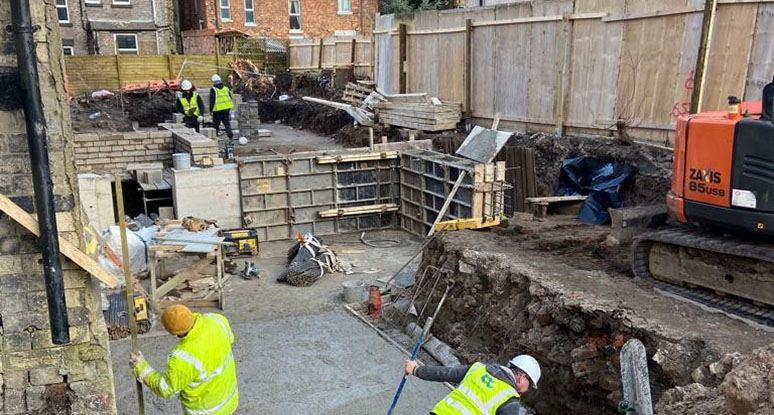 Urbanex groundworks team preparing foundations at a residential construction site in Liverpool with diggers and hi-vis workers.